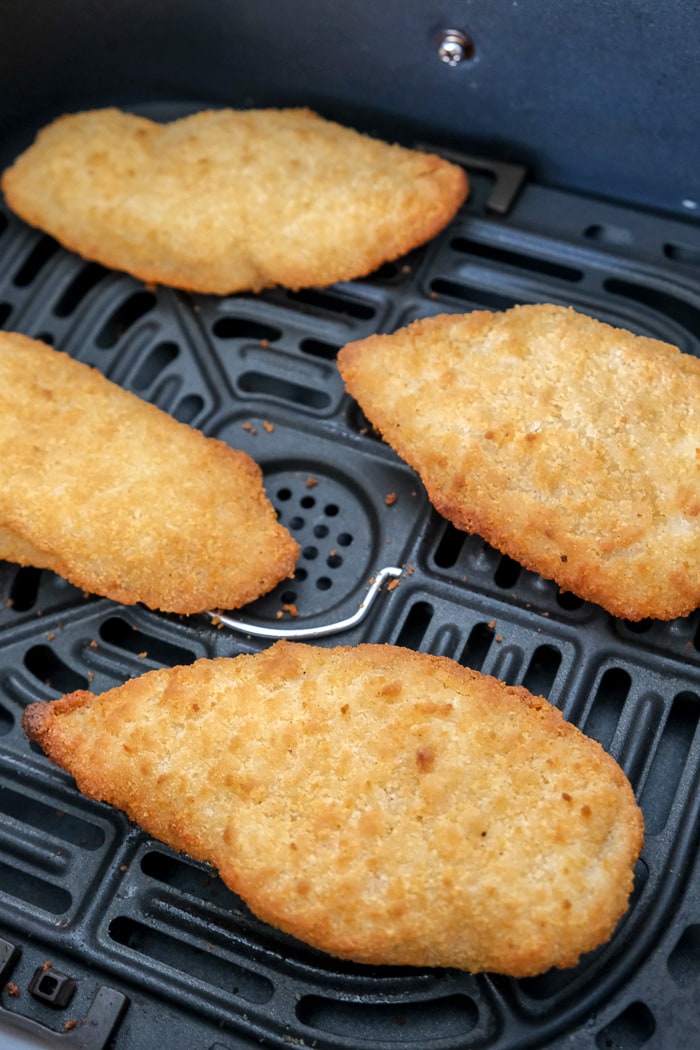 four crispy breaded fish fillets laying on black air fryer tray.