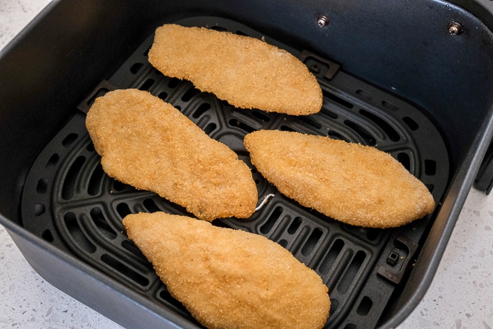 frozen breaded fish fillets in black air fryer tray on white counter top.