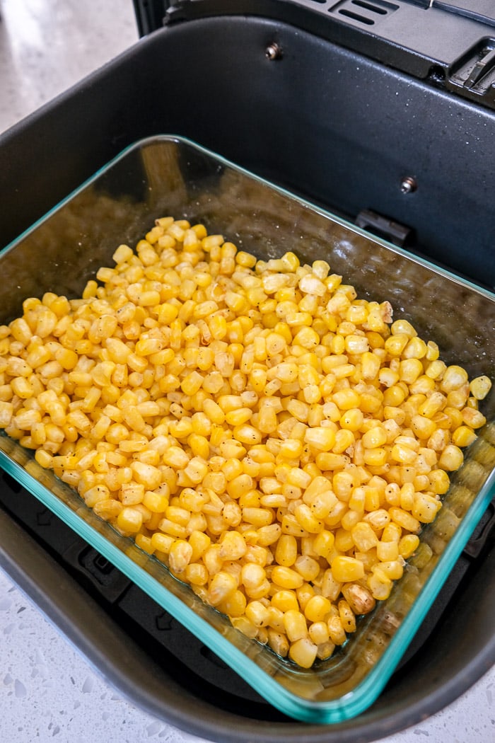 cooked corn in glass dish in black air fryer tray on white counter.