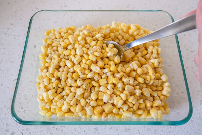 silver spoon in glass dish full of frozen corn on white counter top.
