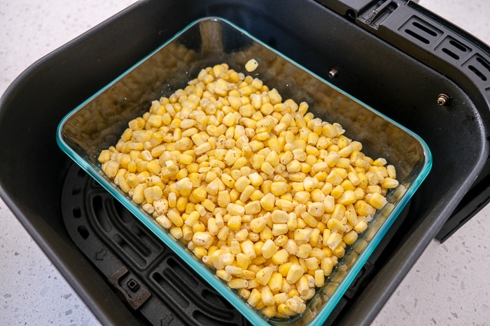 frozen corn in glass dish sitting in black air fryer tray on counter top.