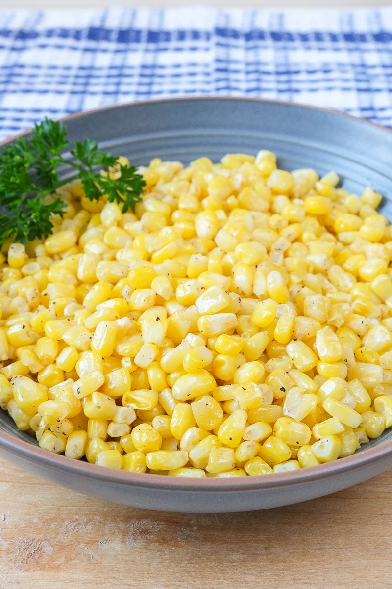 cooked corn kernels in blue bowl on wooden board with blue cloth behind.