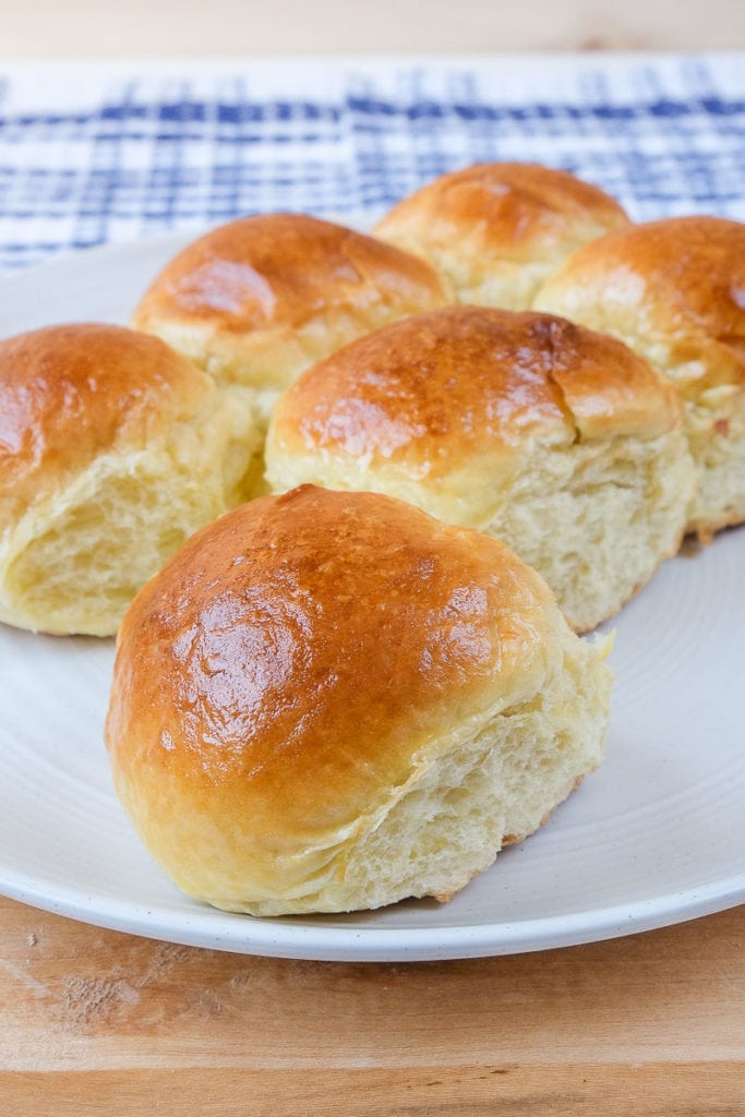 soft golden brown brioche buns on white plate with wooden board underneath.
