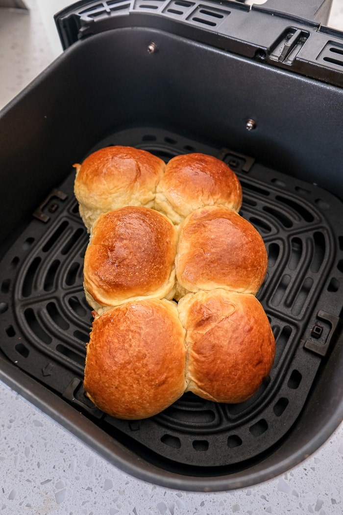 cooked dinner rolls stuck together in black air fryer tray on white counter top.