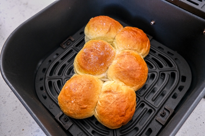 frozen buns on black air fryer tray on white counter.