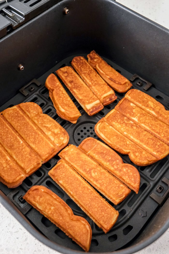 crispy french toast sticks in black air fryer tray on counter top.