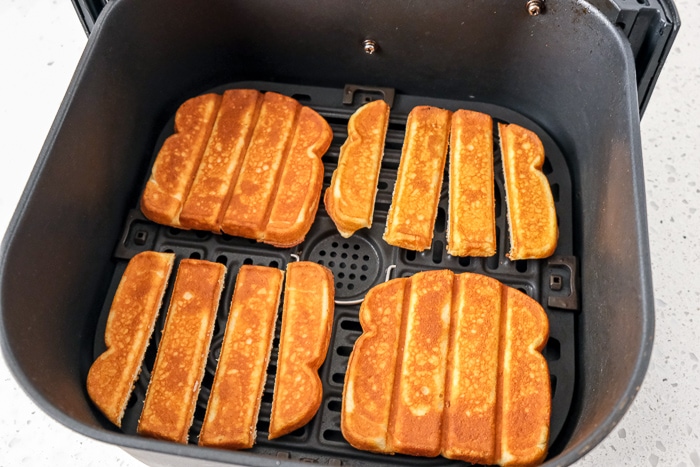 french toast sticks laying in black air fryer tray on white counter.
