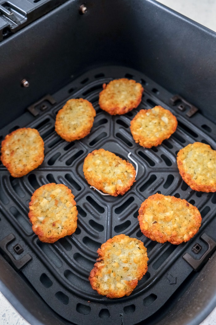 nine crispy potato pancakes laying in black air fryer tray on counter.
