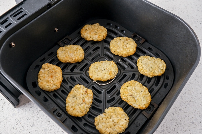 frozen potato pancakes laying in black air fryer tray on white counter top.