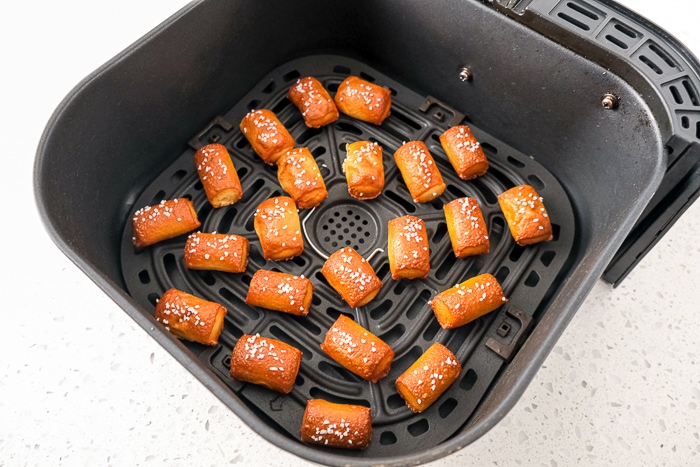 frozen pretzel bites with salt on top in black air fryer tray on white counter.