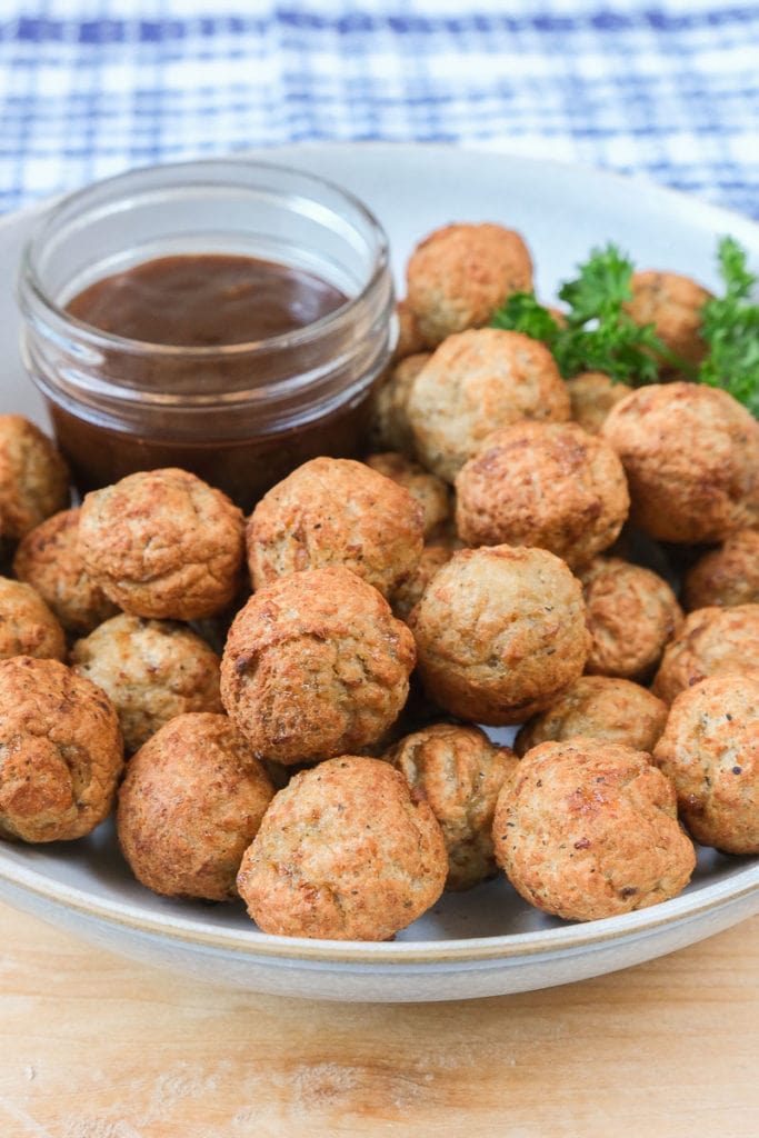 bowl of crispy turkey meatballs with dipping sauce on wooden board with blue cloth behind.