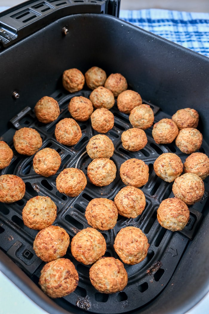 cooked turkey meatballs in black air fryer tray on white counter with blue cloth behind.
