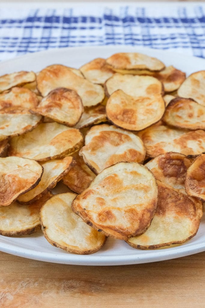 homemade potato chips on plate with blue patterned cloth behind.