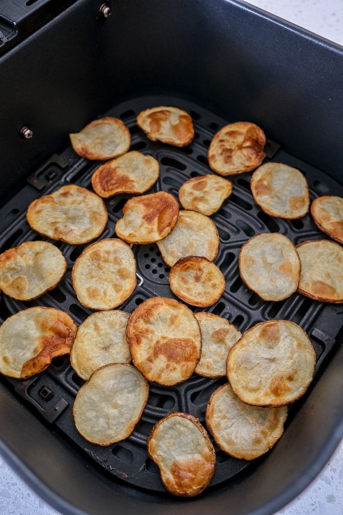 crispy potato chips in black air fryer tray on counter top.