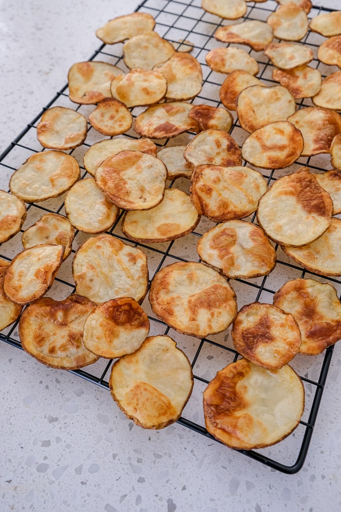 crispy potato chips on cooling rack sitting on white counter.