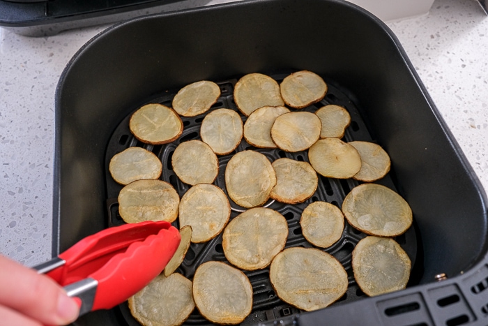 red tongs flipping potato chips in black air fryer tray on counter top.