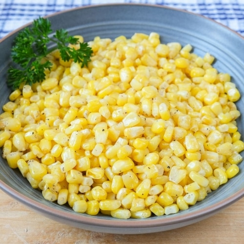 yellow corn kernels with parsley in blue bowl on wooden board.