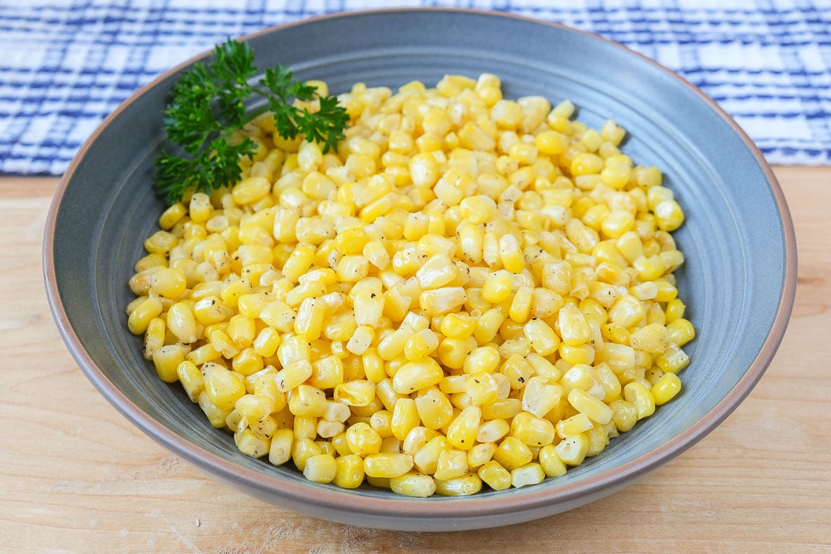 yellow corn kernels with parsley in blue bowl on wooden board.