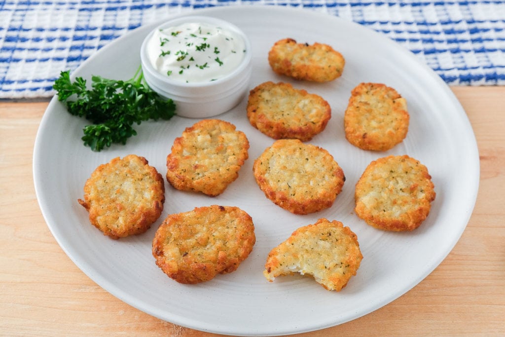 crispy potato pancakes on white plate with sour cream and parsley beside on wooden board.