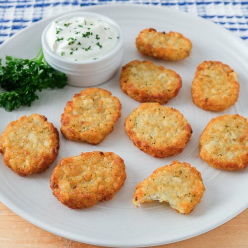 crispy potato pancakes on white plate with sour cream and parsley beside on wooden board.