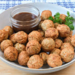 bowl of cooked turkey meatballs on wooden board with blue cloth behind.