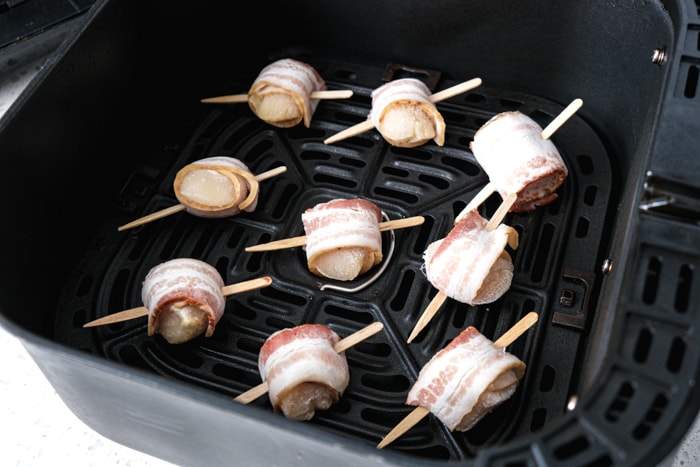 frozen bacon wrapped scallops on black air fryer tray in white counter top.