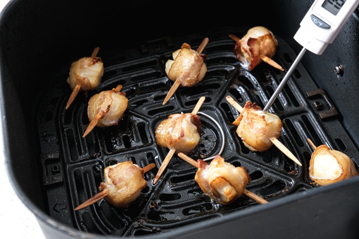 metal tipped thermometer sticking into scallop wrapped in bacon sitting in black air fryer tray.
