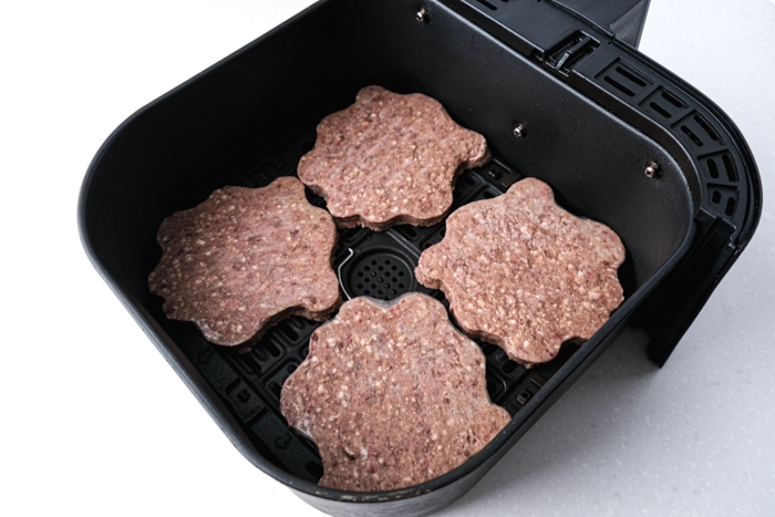 raw frozen burger patties sitting in black air fryer tray on white counter.
