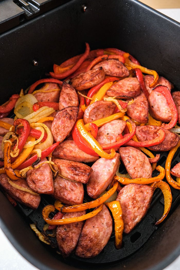cooked kielbasa peppers and onions with spices in black air fryer tray on countertop.