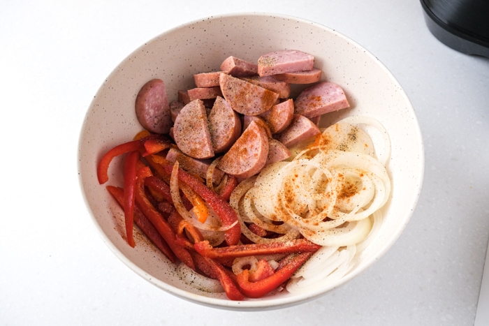 kielbasa peppers and onion in bowl covered in oil and spices.