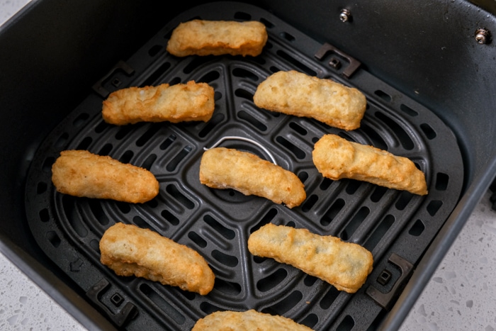 frozen pickle spears with breading in black air fryer tray on white counter.