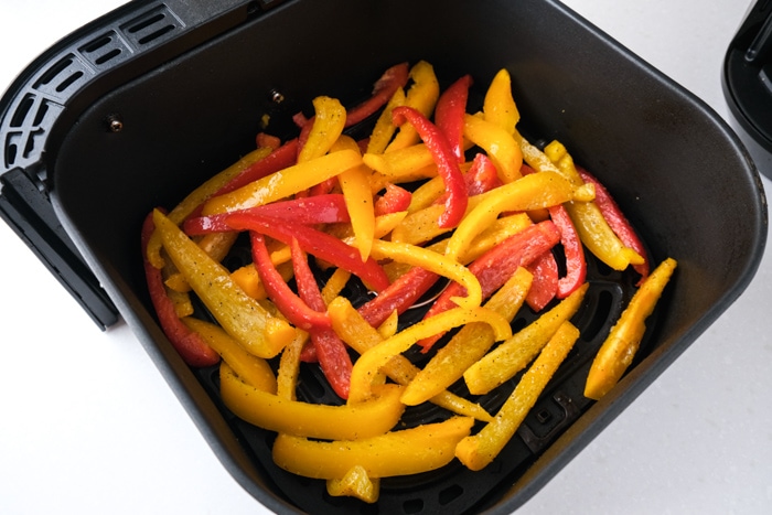 raw strips of red and yellow peppers sitting in black air fryer basket on counter.