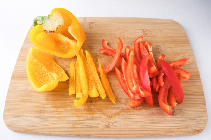 slices of yellow and red peppers on wooden cutting board on white counter top.
