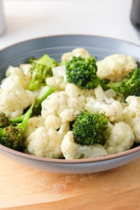 cooked broccoli and cauliflower florets in blue bowl on wooden board on counter.