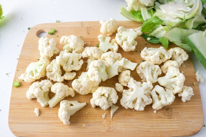 white florets of cauliflower on wooden board on white counter.