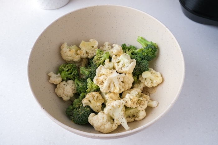 small florets of cauliflower and broccoli covered in spices in white mixing bowl on counter.