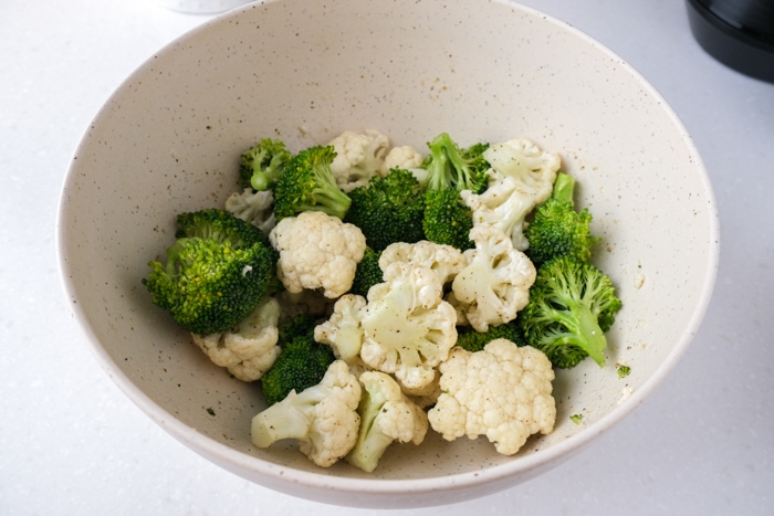 broccoli and cauliflower florets coated in oil and spices in white bowl on counter.