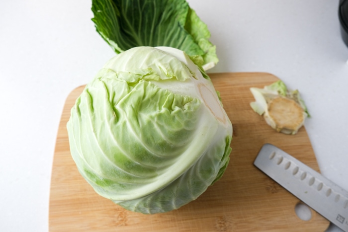 head of cabbage with stem cut off on wooden board sitting on white countertop.