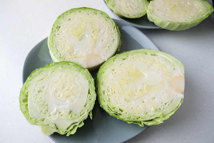 three raw cabbage steaks on blue plate sitting on white countertop.