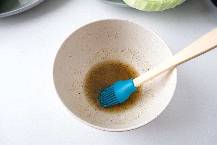 white bowl with oil and spices mixed together with blue tipped brush sticking out on counter.
