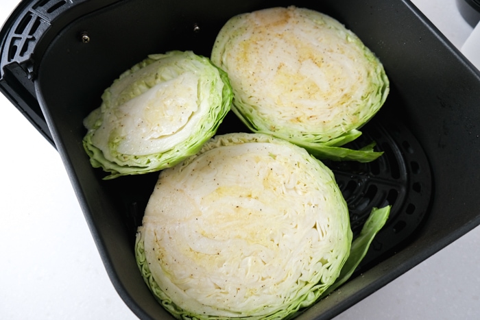 raw cabbage steaks sitting in black air fryer tray on counter.