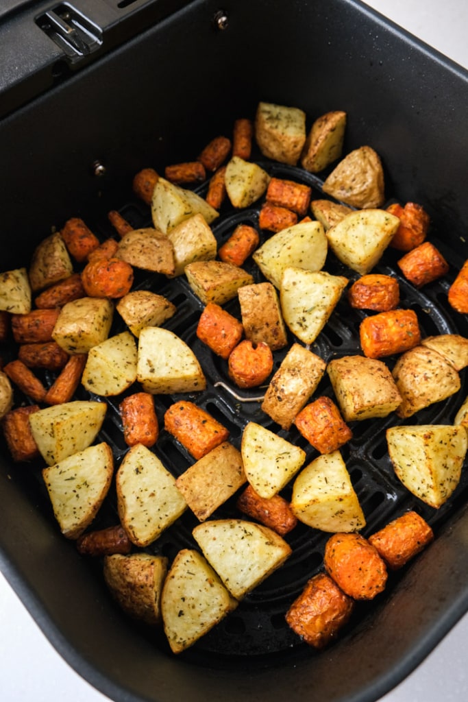 roasted spiced carrots and potatoes in black air fryer tray on white counter.