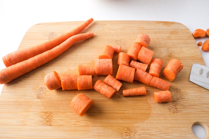 raw carrots cut up on wooden cutting board sitting on white counter top.