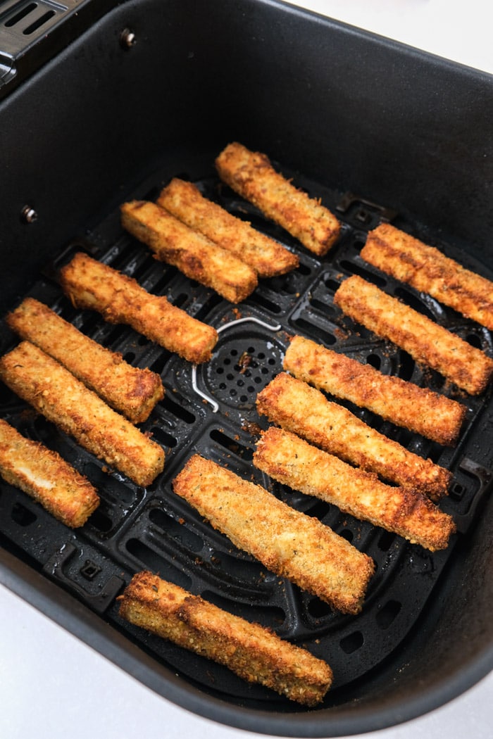 crispy eggplant fries sitting in two rows in black air fryer basket on counter.