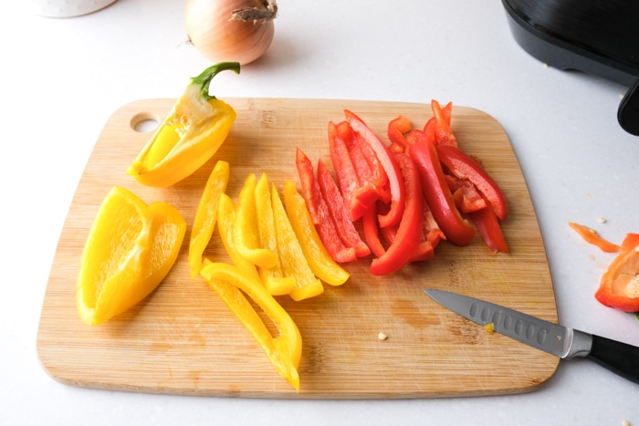 strips of yellow and red peppers cut on wooden cutting board with knife beside on counter.