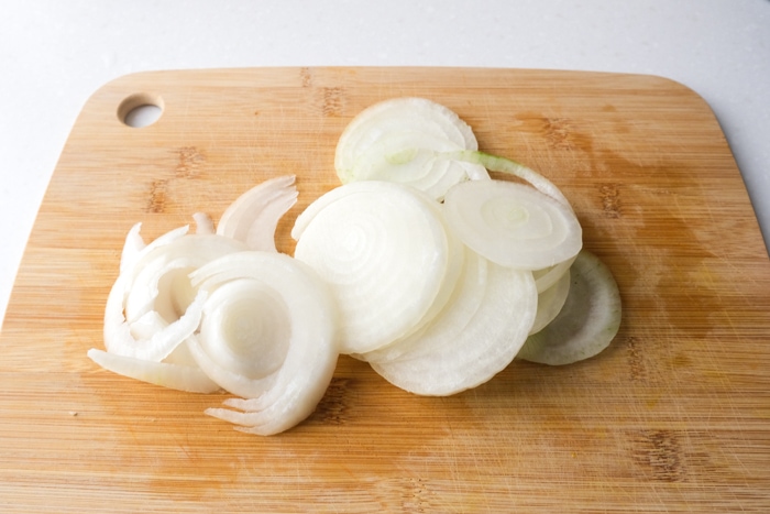 slices of white onion cut on wooden board sitting on white counter.