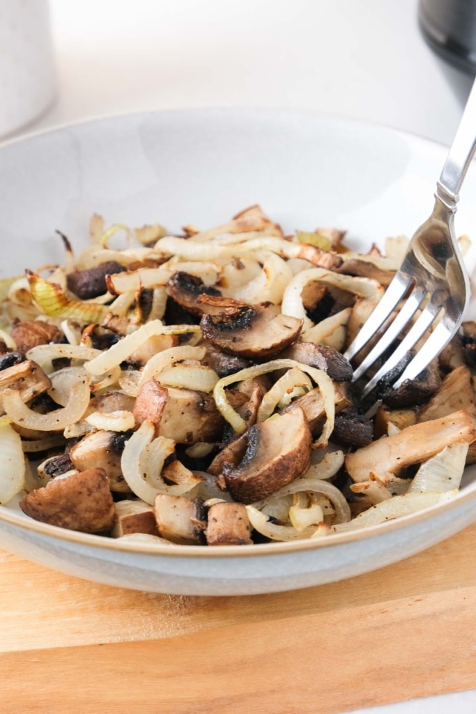 mushrooms and onions cooked sitting in bowl on wood with fork sticking out.