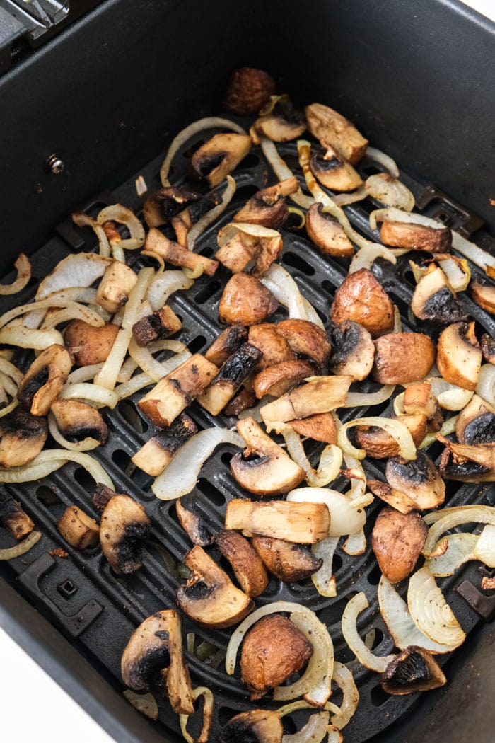 cooked mushrooms and onions in black air fryer tray.