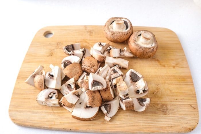 mushroom chopped into pieces on wooden cutting board on white kitchen counter.