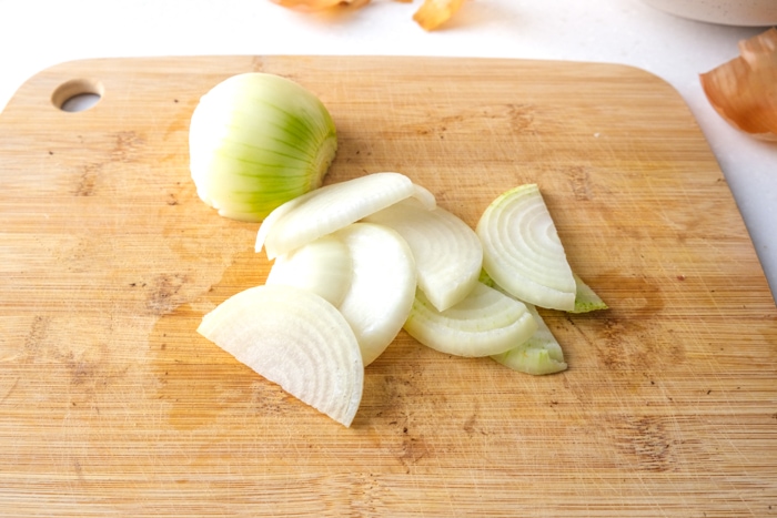 white onion cut into slices with half piece behind on wooden cutting board.